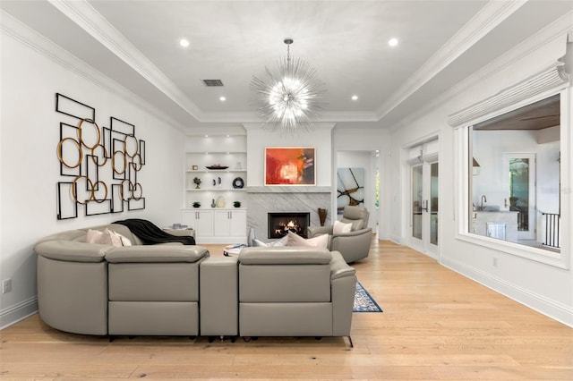 living room with a high end fireplace, light wood-type flooring, ornamental molding, sink, and a chandelier