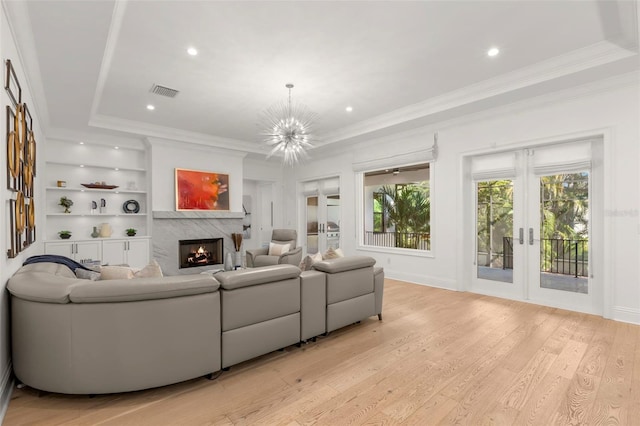 living room with a fireplace, light wood-type flooring, crown molding, an inviting chandelier, and french doors