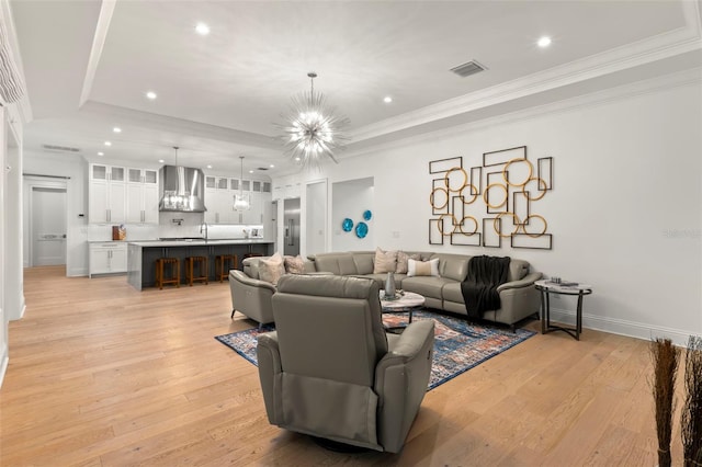 living room with light hardwood / wood-style flooring, a chandelier, a tray ceiling, and crown molding