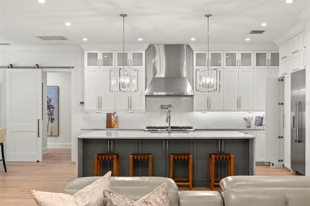 kitchen featuring a kitchen breakfast bar, a center island with sink, pendant lighting, and wall chimney range hood