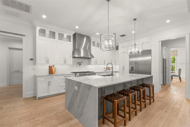 kitchen with white cabinets, sink, a center island with sink, wall chimney exhaust hood, and light hardwood / wood-style flooring