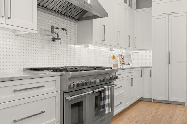 kitchen featuring light hardwood / wood-style floors, tasteful backsplash, white cabinetry, custom exhaust hood, and double oven range