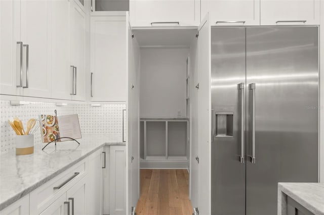 kitchen with light wood-type flooring, white cabinetry, decorative backsplash, high end fridge, and light stone countertops