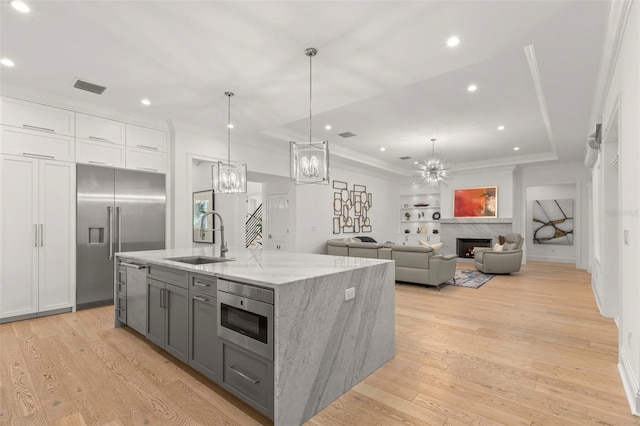 kitchen with light wood-type flooring, sink, a center island with sink, decorative light fixtures, and light stone countertops