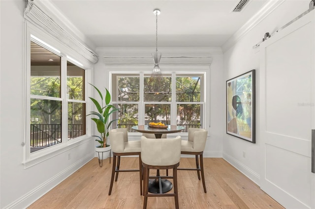 dining area featuring light hardwood / wood-style flooring, ornamental molding, and a barn door