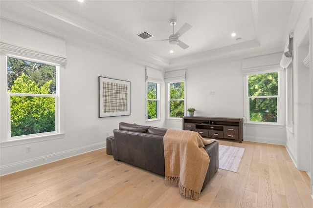 living room with light wood-type flooring, ceiling fan, a raised ceiling, and plenty of natural light