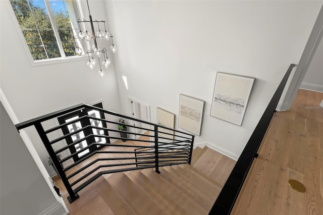 staircase with wood-type flooring and an inviting chandelier