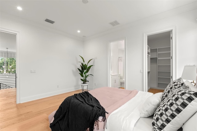 bedroom featuring a closet, crown molding, a walk in closet, hardwood / wood-style flooring, and ensuite bath