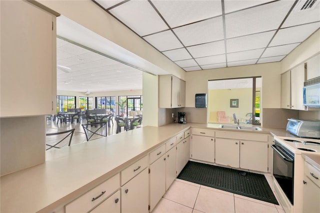 kitchen featuring sink, range with electric stovetop, cream cabinetry, light tile patterned flooring, and kitchen peninsula