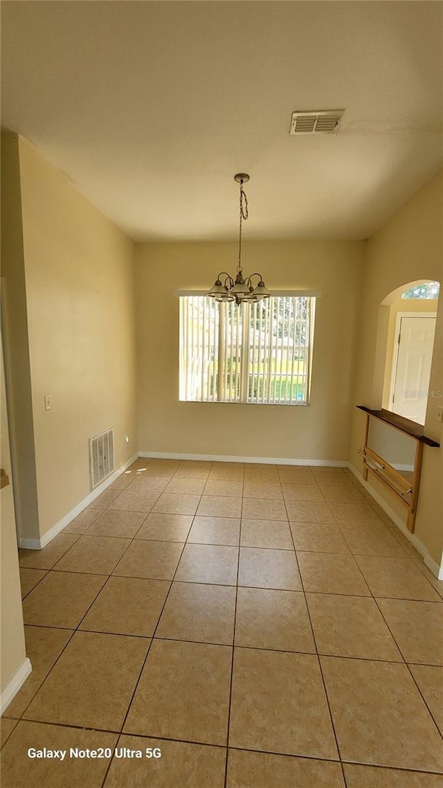 tiled empty room featuring a chandelier