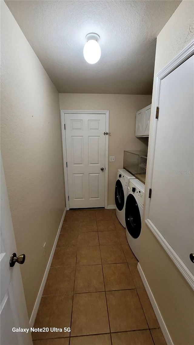 laundry room with dark tile patterned floors, a textured ceiling, cabinets, and separate washer and dryer