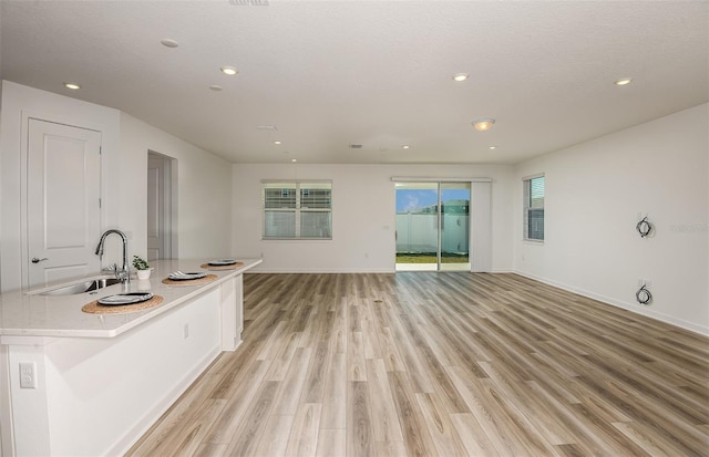 interior space with a sink, baseboards, open floor plan, light countertops, and light wood-type flooring