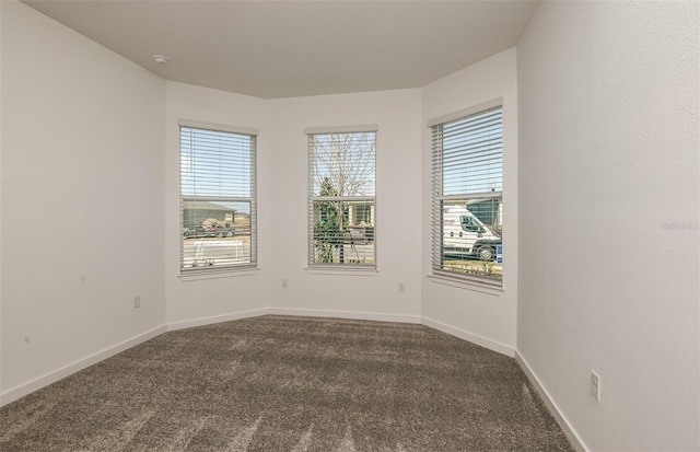 unfurnished room with baseboards and dark colored carpet