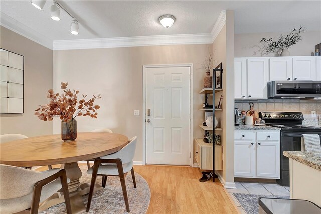 dining space featuring light wood-type flooring, a textured ceiling, ornamental molding, and track lighting