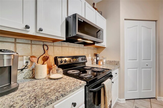 kitchen featuring light tile patterned flooring, light stone counters, white cabinets, backsplash, and black electric range oven