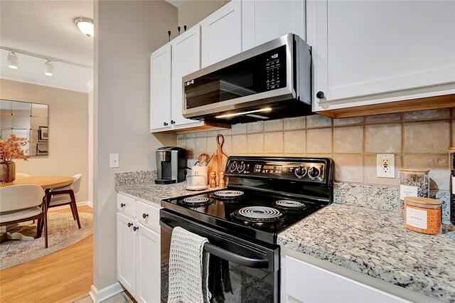 kitchen featuring light wood-type flooring, black electric range, tasteful backsplash, white cabinets, and light stone countertops