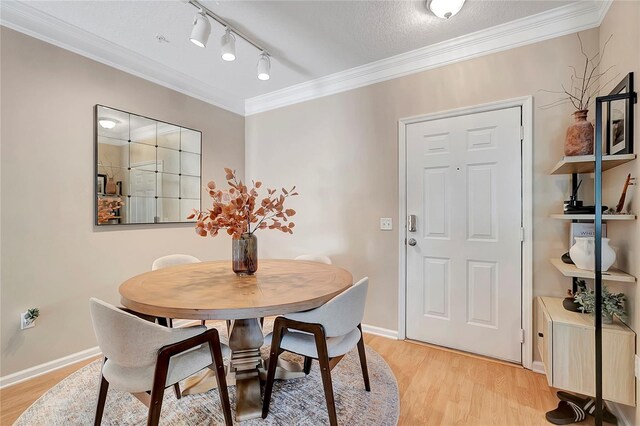 dining area featuring a textured ceiling, crown molding, light hardwood / wood-style flooring, and rail lighting