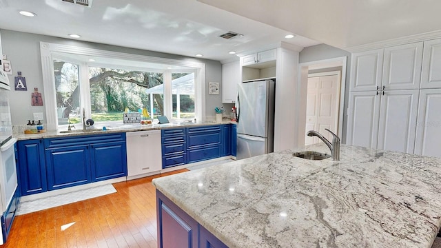 kitchen with stainless steel refrigerator, light hardwood / wood-style flooring, white dishwasher, and blue cabinetry