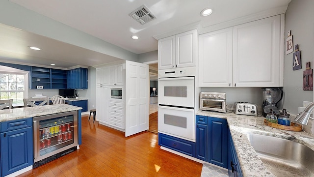 kitchen with blue cabinets, wine cooler, sink, white cabinetry, and double oven