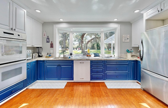 kitchen with blue cabinets, white cabinets, sink, white appliances, and light hardwood / wood-style flooring