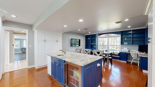 kitchen with blue cabinets, a kitchen island with sink, hardwood / wood-style floors, and white cabinetry