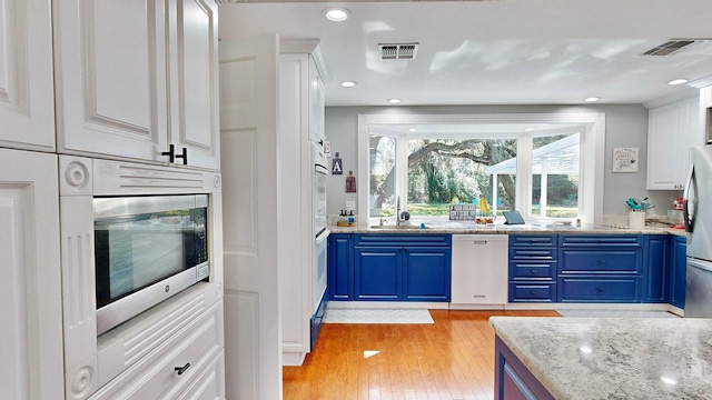 kitchen with white cabinets, blue cabinets, appliances with stainless steel finishes, and light wood-type flooring