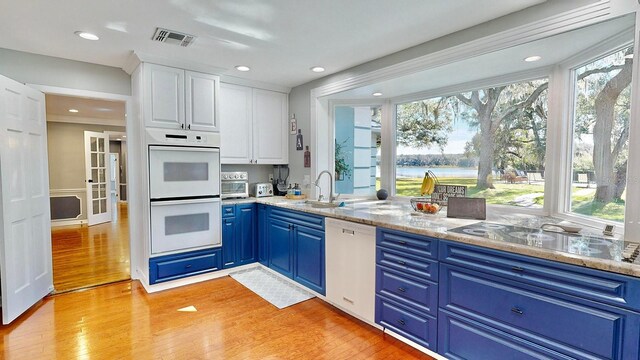 kitchen with light wood-type flooring, plenty of natural light, white appliances, and white cabinetry