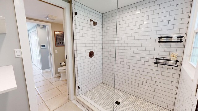 bathroom featuring toilet, a shower with door, and tile patterned floors