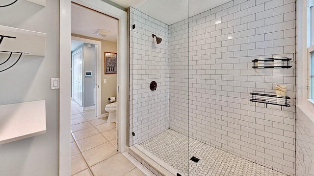 bathroom with tiled shower, toilet, and tile patterned floors