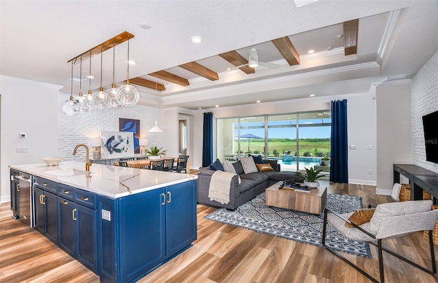 kitchen featuring an island with sink, ceiling fan with notable chandelier, pendant lighting, blue cabinetry, and light hardwood / wood-style flooring