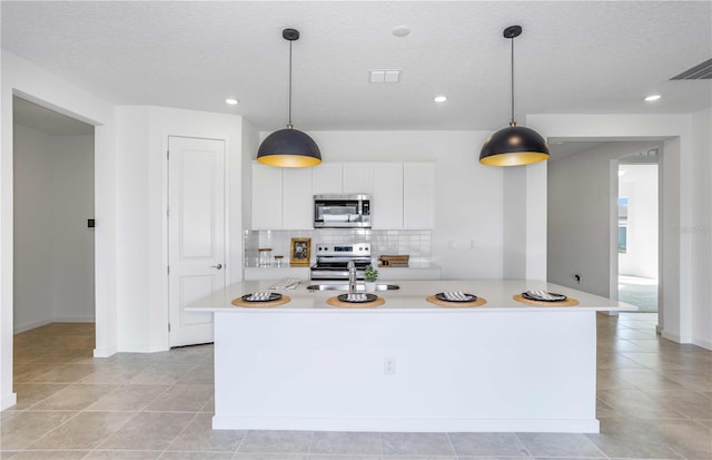 kitchen featuring pendant lighting, stainless steel appliances, white cabinets, a center island with sink, and decorative backsplash