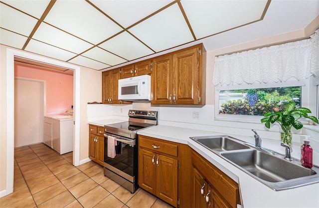 kitchen with electric stove, brown cabinets, white microwave, a sink, and separate washer and dryer