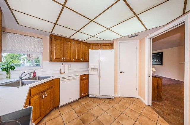 kitchen with light countertops, visible vents, brown cabinetry, a sink, and white appliances