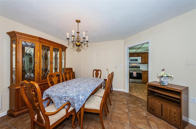 dining room with a chandelier, dark tile patterned flooring, and baseboards