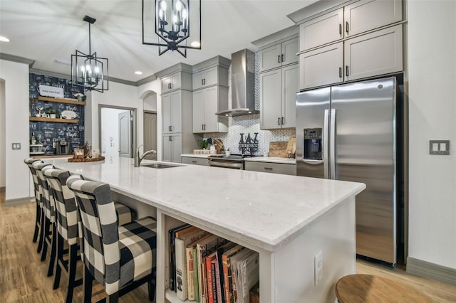 kitchen with wall chimney range hood, sink, appliances with stainless steel finishes, and a large island with sink