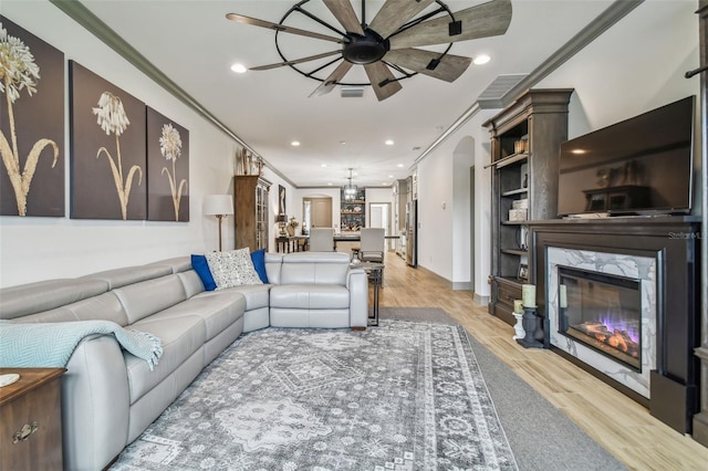 living room featuring ceiling fan, ornamental molding, light hardwood / wood-style flooring, and a high end fireplace