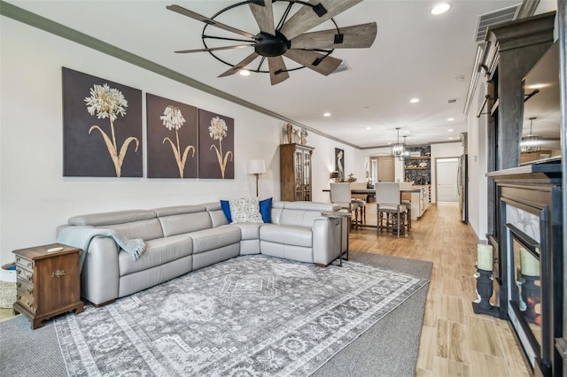 living room with ornamental molding, light wood-type flooring, and ceiling fan with notable chandelier