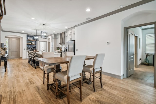 dining area with a healthy amount of sunlight, ornamental molding, a chandelier, and light wood-type flooring