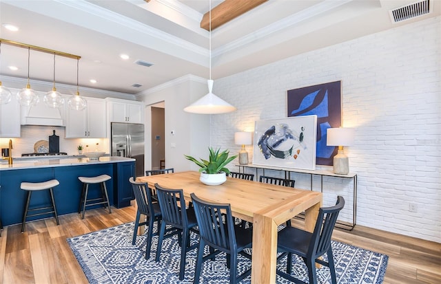 dining room with brick wall, ornamental molding, and light hardwood / wood-style floors