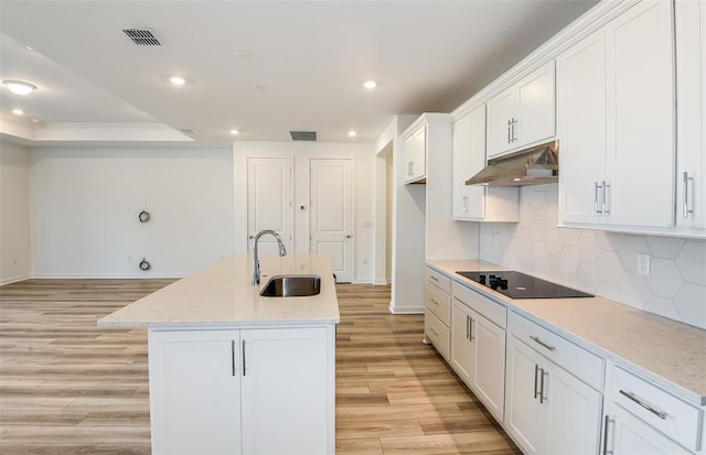 kitchen featuring visible vents, a sink, light wood-style floors, under cabinet range hood, and black electric stovetop