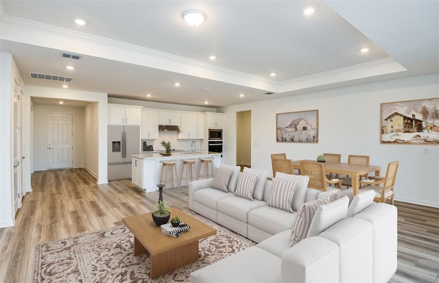 living area featuring ornamental molding, a tray ceiling, light wood-type flooring, and visible vents