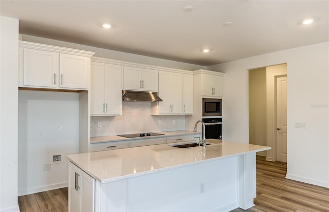 kitchen featuring under cabinet range hood, built in microwave, white cabinets, and a sink