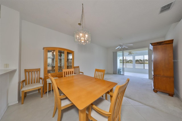 dining room with ceiling fan with notable chandelier, a textured ceiling, light tile patterned floors, and a water view