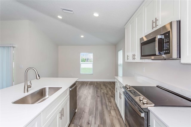 kitchen with appliances with stainless steel finishes, white cabinetry, a textured ceiling, light wood-type flooring, and sink