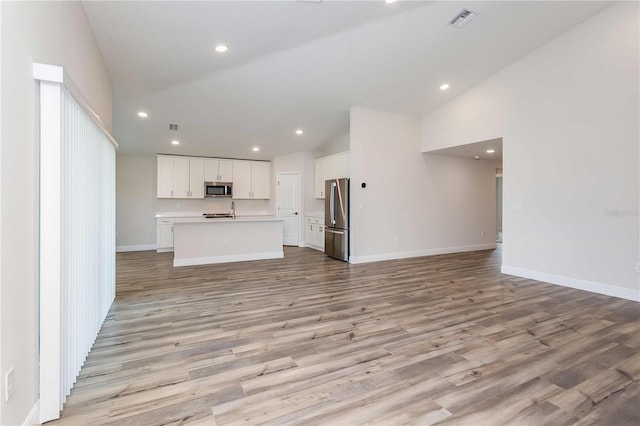 unfurnished living room with light hardwood / wood-style floors, sink, and high vaulted ceiling