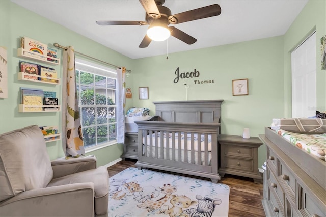 bedroom with ceiling fan, a crib, and dark hardwood / wood-style flooring