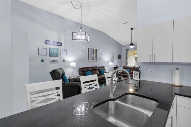 kitchen with sink, white cabinets, vaulted ceiling, an inviting chandelier, and decorative light fixtures