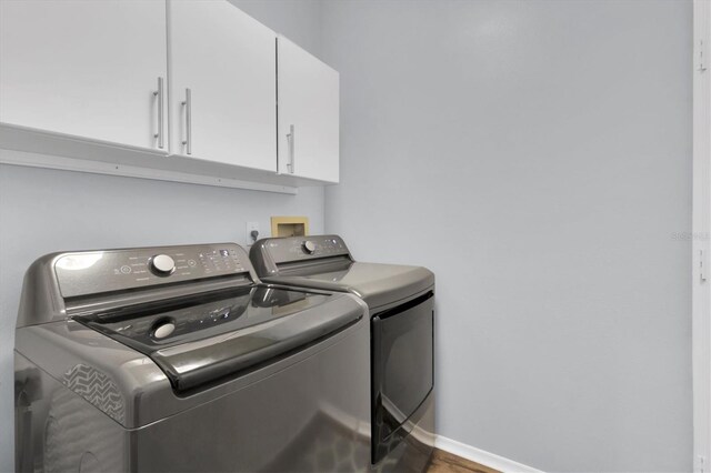 clothes washing area with washing machine and clothes dryer and cabinets