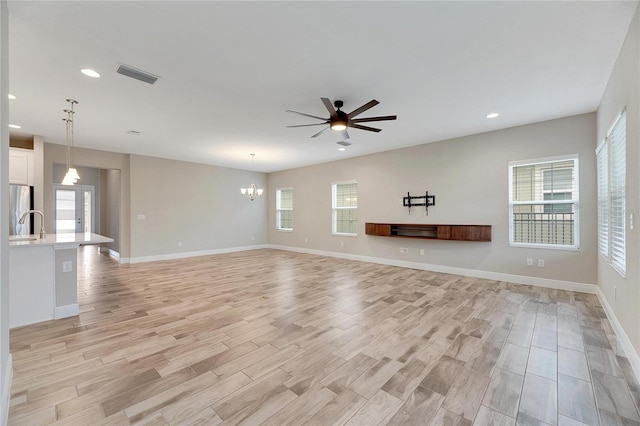 unfurnished living room featuring ceiling fan with notable chandelier and light hardwood / wood-style floors