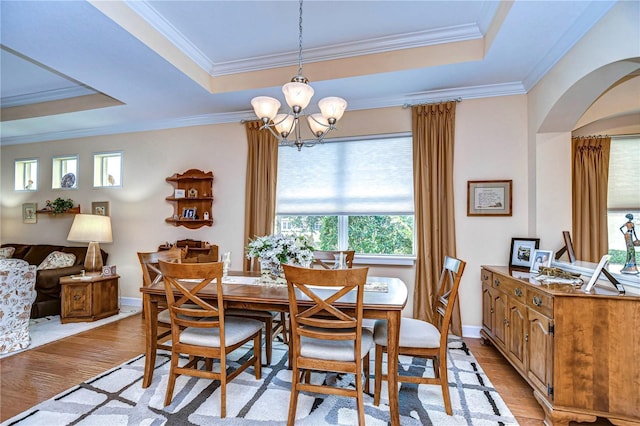 dining space featuring a raised ceiling, crown molding, and light wood-type flooring